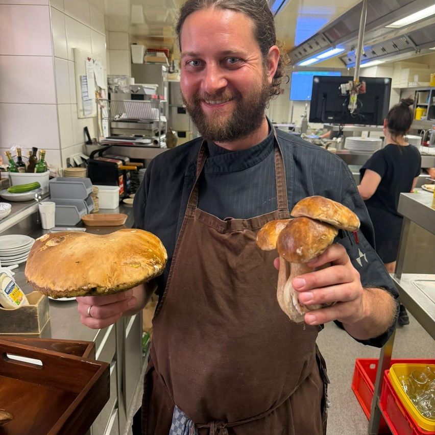A chef in a kitchen holds two large mushrooms, smiling for the camera.
