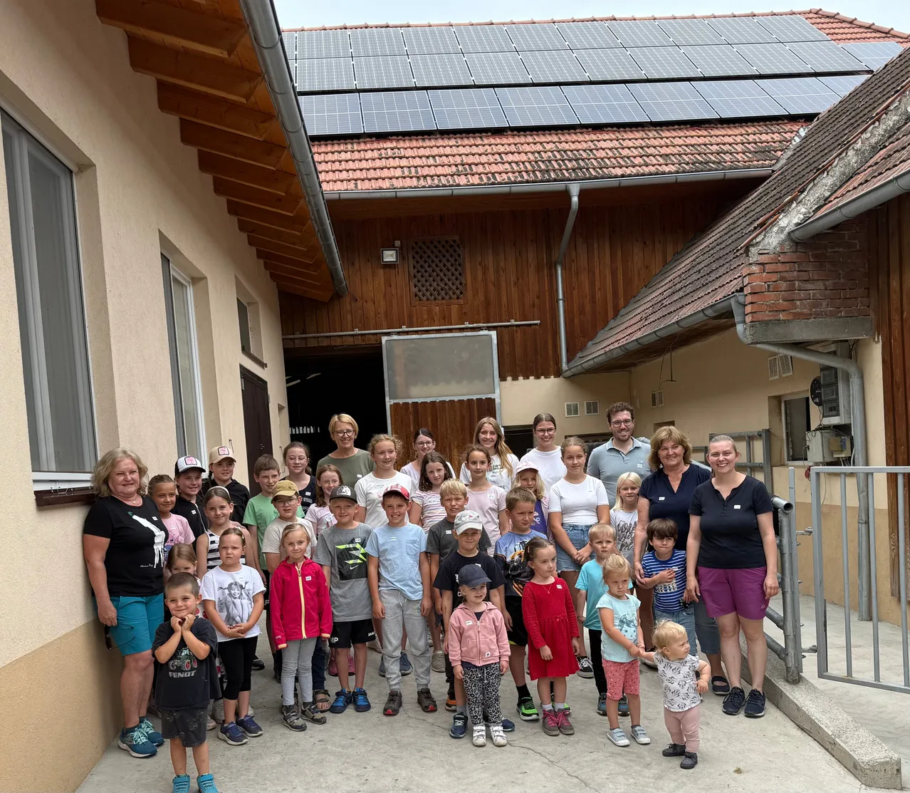 Eine Gruppe von Kindern und Erwachsenen steht vor einem Haus mit Solarmodulen auf dem Dach. Sie alle lächeln und scheinen für ein Gruppenfoto zu posieren.