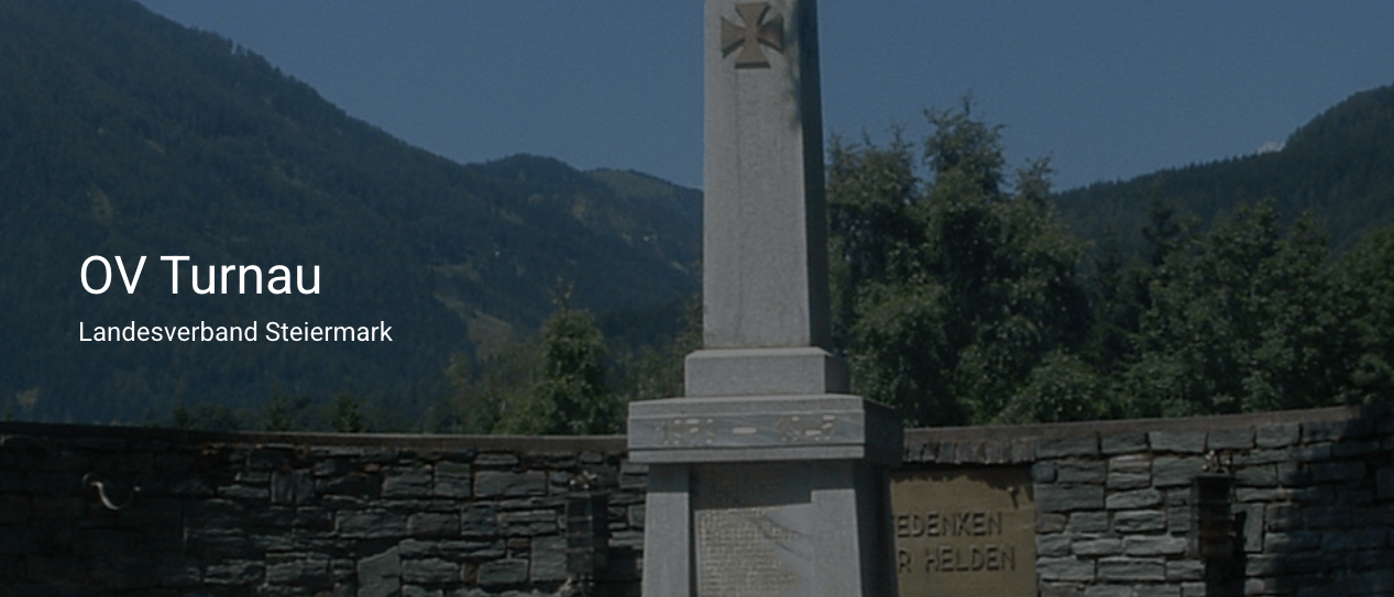 Ein Steindenkmal mit einer Inschrift, das ein Kreuzsymbol zeigt, umgeben von Grün und Bergen.