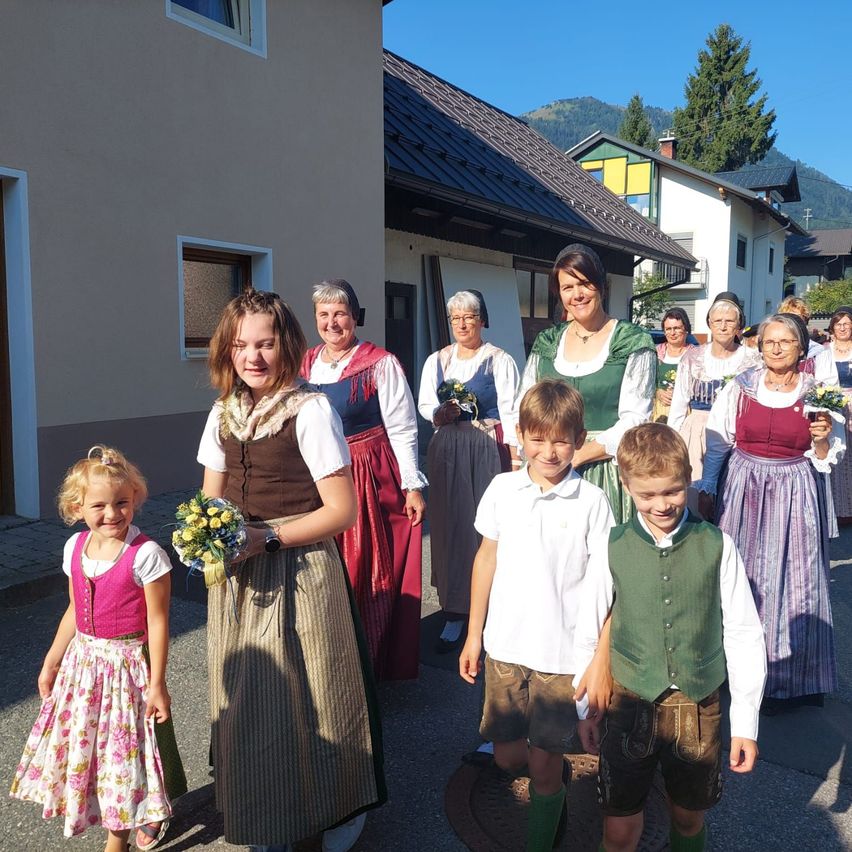 Eine Gruppe von Menschen in traditioneller Kleidung steht vor einem Gebäude. Einige halten Blumen.
