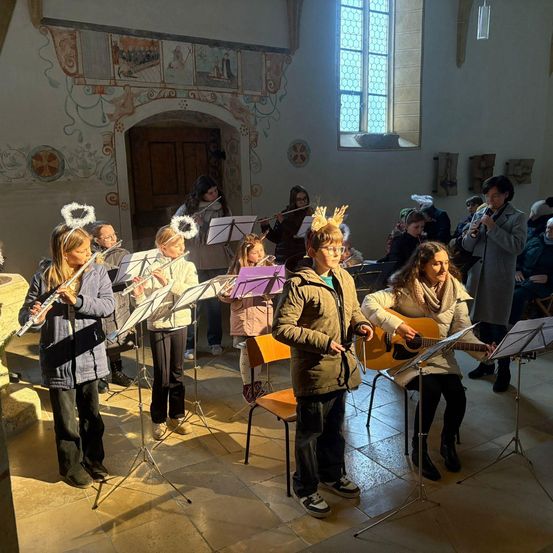 Eine Gruppe von Kindern und Erwachsenen spielt Musikinstrumente in einer Kirche. Einige halten Flöten und andere haben Gitarren.