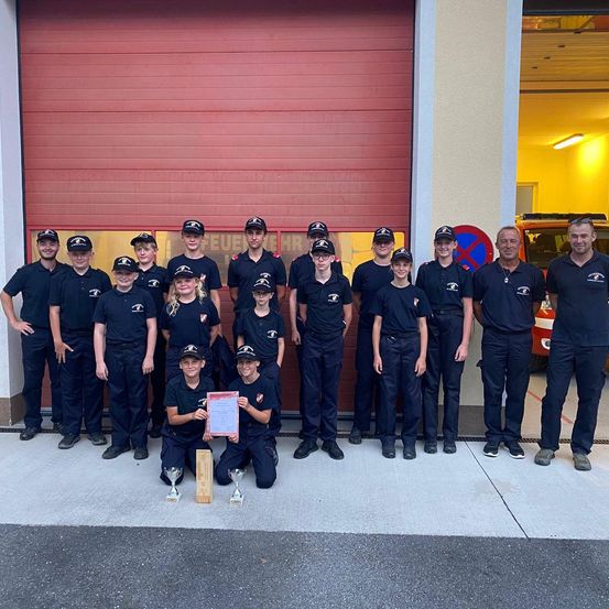 Eine Gruppe junger Menschen in Uniform steht vor einer Feuerwache, hält Auszeichnungen und posiert für ein Foto.