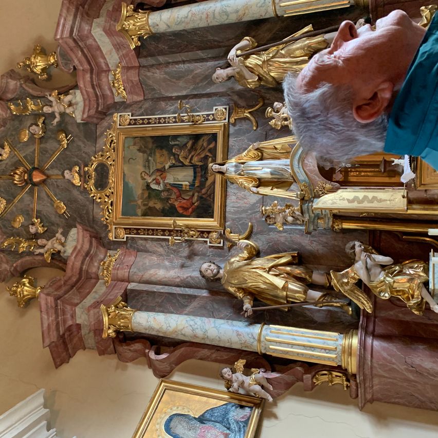 Ein älterer Mann schaut auf goldene Statuen und Gemälde an einem Kirchenaltar. Die Gemälde und Statuen sind vergoldet und die Wand ist aus Marmor.