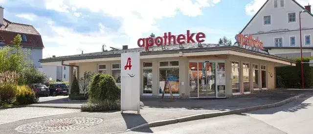 Ein Apothekengebäude mit dem Schild 'apotheke' oben und der Nummer '4' an der Seite. Autos sind davor geparkt.