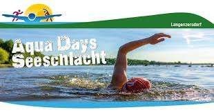 Ein Bild eines Schwimmers in einem See oder Fluss mit den Worten Aqua Days Seeschlacht oben. Der Schwimmer trägt eine rote Mütze und Schwimmbrille. Der Himmel ist klar, und es gibt Bäume in der Ferne.