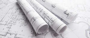 Drei aufgerollte Architekturpläne liegen auf einer weißen Oberfläche mit einem Grundrissdesign. Die Pläne sind aufgerollt und haben Text und Diagramme. Der Grundriss ist detailliert mit verschiedenen Linien und Formen.