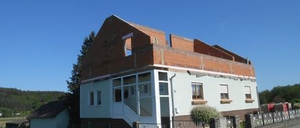 Ein zweistöckiges Gebäude im Bau mit einem braunen Dach und weißen Wänden. Es hat mehrere Fenster und eine Treppe an der Seite. Das Gebäude ist von einem Zaun umgeben und befindet sich in einem Grasbereich.