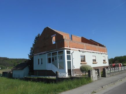 Ein zweistöckiges Gebäude im Bau mit einem braunen Dach und weißen Wänden. Es hat mehrere Fenster und eine Treppe an der Seite. Das Gebäude ist von einem Zaun umgeben und befindet sich in einem Grasbereich.