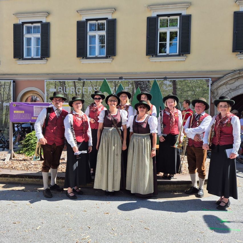 Eine Gruppe von Menschen in traditioneller Kleidung posiert für ein Foto vor einem Gebäude mit mehreren Fenstern und einem Schild, das Burgers steht.
