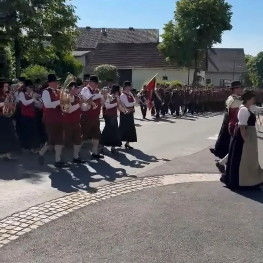 Eine Blaskapelle in traditioneller Kleidung spielt Blechblasinstrumente auf der Straße bei einem Umzug.
