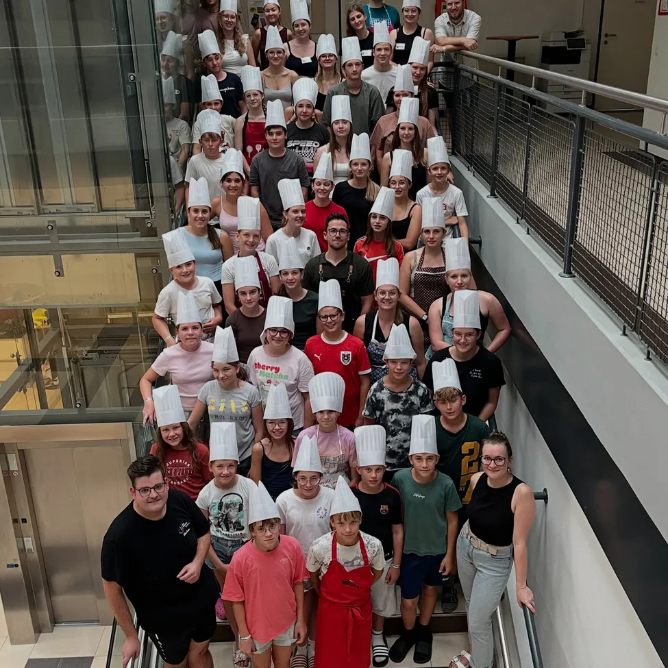 Eine Gruppe von Menschen, einschließlich Kindern und Erwachsenen, trägt Kochmützen und posiert für ein Foto auf einer Treppe.