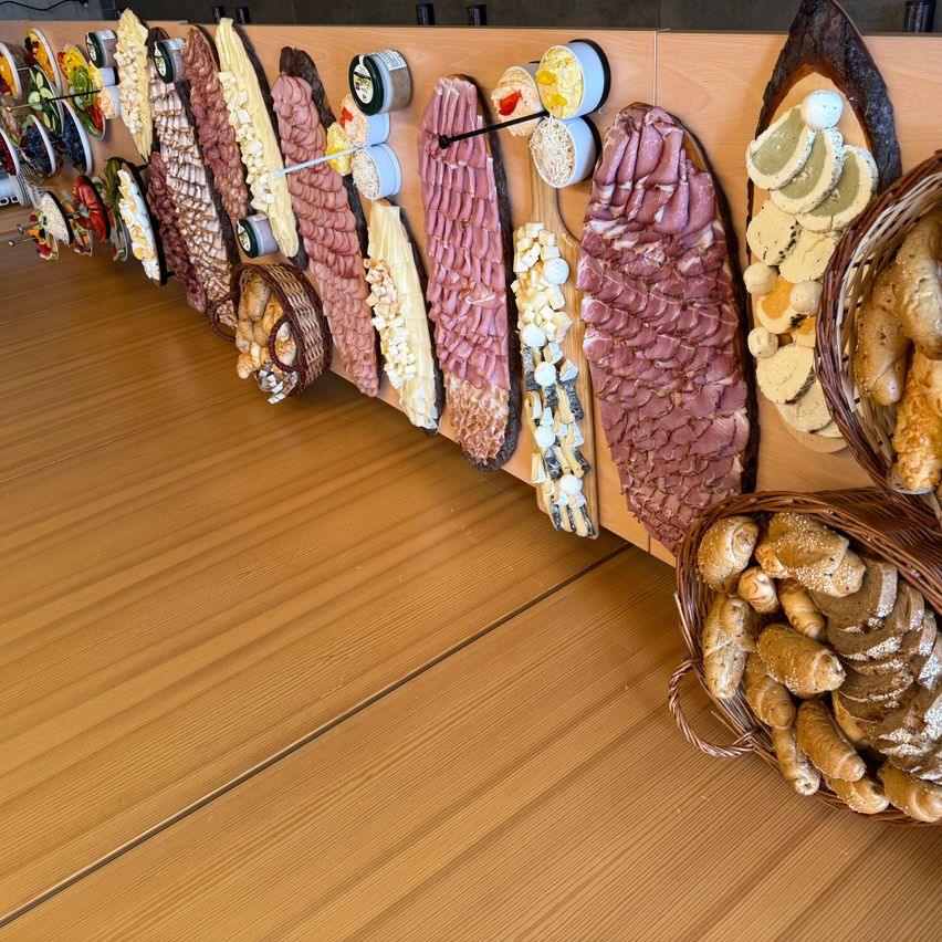 Auf einem Holztisch ist eine Auswahl an Charcuterie mit verschiedenen Fleischsorten, Käse und Aufstrichen auf Holzbrettern und in Körben zu sehen.