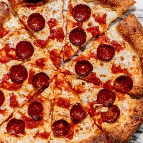 Eine runde Pizza mit Käse und Peperoni, in acht Stücke geschnitten, auf einer Marmoroberfläche. Die Pizza hat einen goldbraunen Rand.