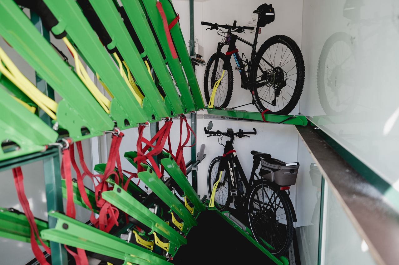 A storage area with bikes on a rack, secured with red straps. One bike has a helmet and a bag. The bikes are black with various components.