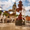 Ein Brunnen auf einem Stadtplatz mit einem Glockenturm im Hintergrund. Ein Radfahrer fährt an einem sonnigen Tag vorbei.