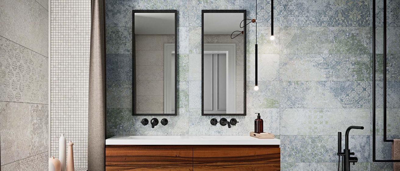 Ein modernes Badezimmer mit einem hölzernen Waschtisch und zwei großen Spiegeln darüber, die eine geflieste Wand und eine Tür reflektieren.