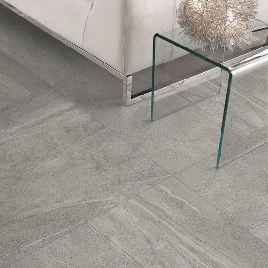 Ein modernes Wohnzimmer mit einer weißen Couch, grau gefliestem Boden und einem Glastisch mit einer dekorativen Lampe.