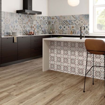 Eine moderne Küche mit Holzboden und gemusterten Fliesen an den Wänden. Es gibt eine Arbeitsplatte mit Wasserhahn und einen braunen Stuhl davor.