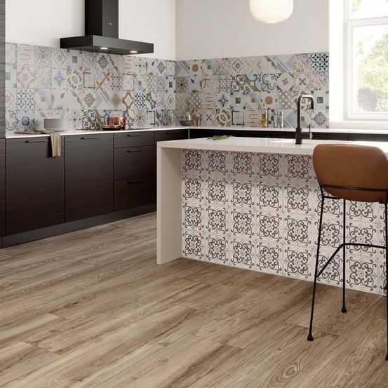 Eine moderne Küche mit Holzboden und gemusterten Fliesen an den Wänden. Es gibt eine Arbeitsplatte mit Wasserhahn und einen braunen Stuhl davor.