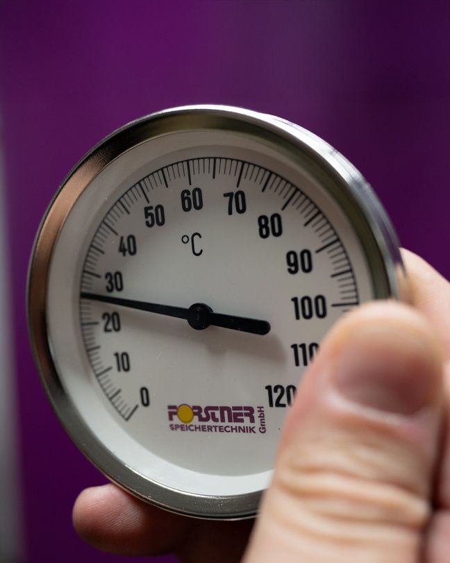 A person holds a thermometer labeled Forster. The scale ranges from 0 to 120 degrees Celsius. The needle points to approximately 60 degrees Celsius.