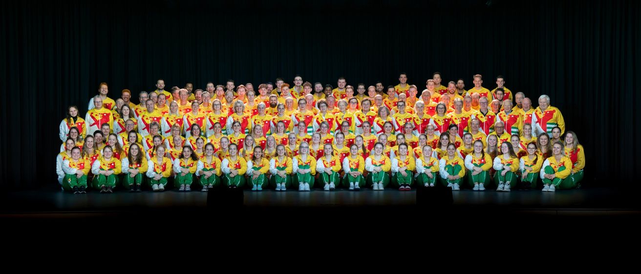 A large group of people in yellow and red uniforms poses for a photo on stage.