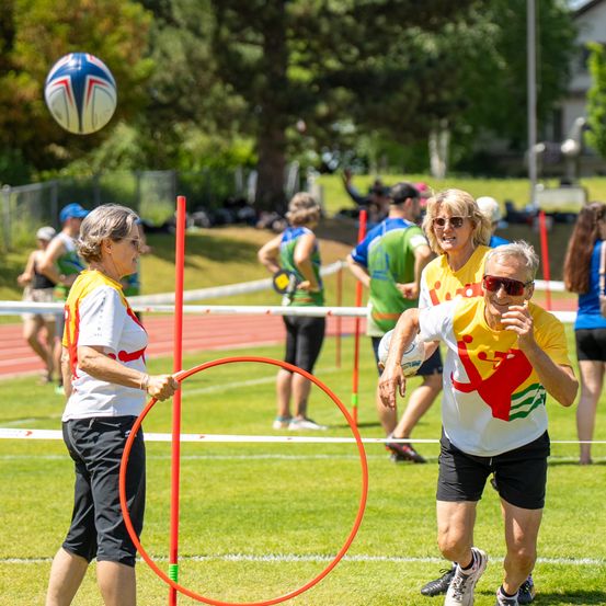 Eine Gruppe älterer Erwachsener spielt ein Spiel mit einem Ball und einem Reifen auf einem Rasenfeld.
