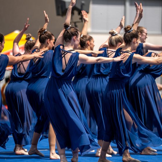 Eine Gruppe von Frauen in blauen Kleidern führt eine synchronisierte Tanzaufführung auf einer blauen Bühne auf.
