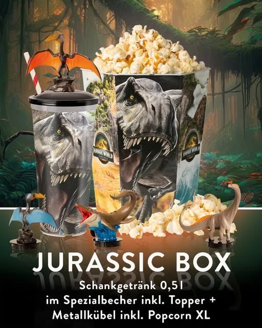 Eine Jurassic Box mit Popcorn, einem Becher, einem Metallbecher und Dinosaurierfiguren. Der Becher hat einen Dinosaurier darauf.