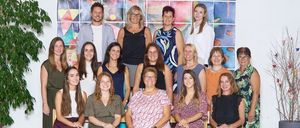 Eine Gruppe von Frauen und einem Mann posiert für ein Foto in einem Raum mit dekorativen Wänden und Topfpflanzen.