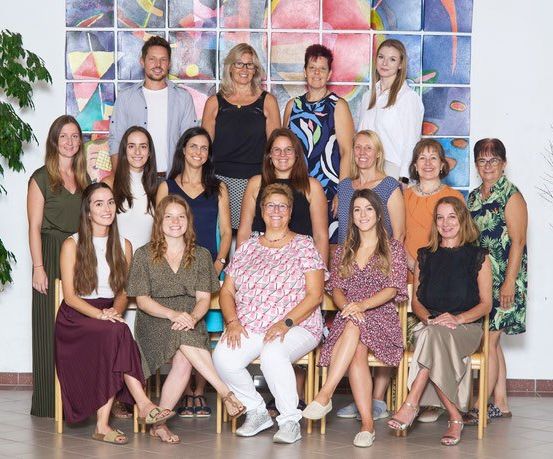 Eine Gruppe von Frauen und einem Mann posiert für ein Foto in einem Raum mit einer farbenfrohen Wand und einer Pflanze.