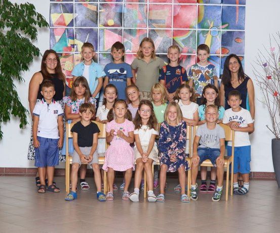 Eine Gruppe von Kindern und zwei Frauen, die für ein Foto vor einer farbenfrohen Wand und Topfpflanzen stehen.