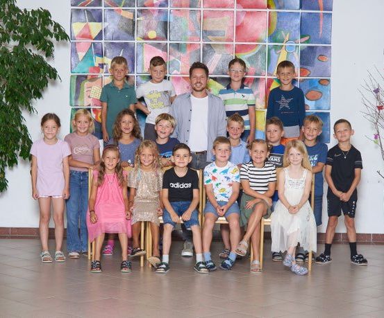 Eine Gruppe von Kindern und einem Mann posiert für ein Foto vor einer bunten Wandmalerei.