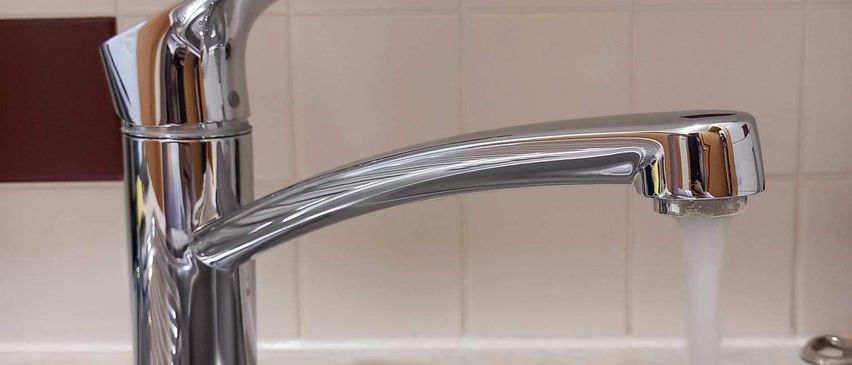 Ein moderner Edelstahl-Küchenhahn mit Wasserfluss, der sich über einem Edelstahlspülbecken befindet.