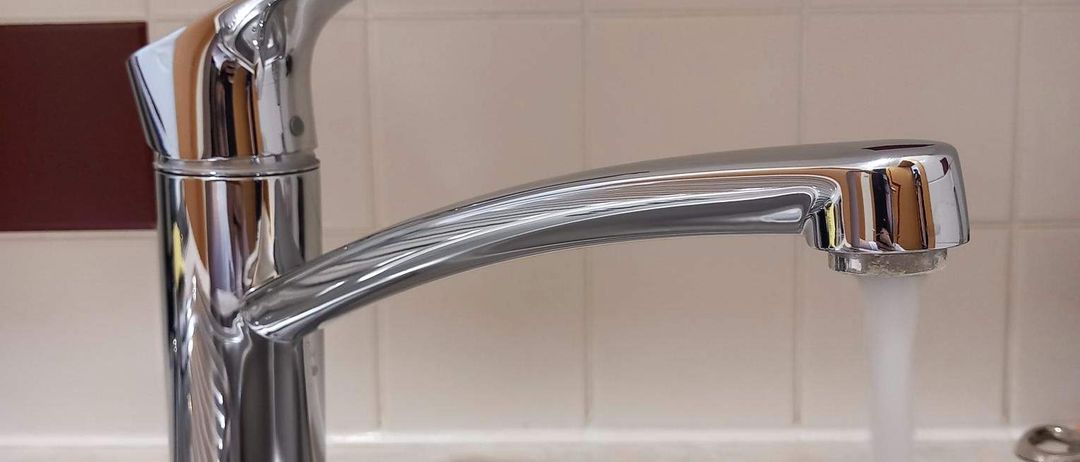 Ein moderner Edelstahl-Küchenhahn mit Wasserfluss, der sich über einem Edelstahlspülbecken befindet.