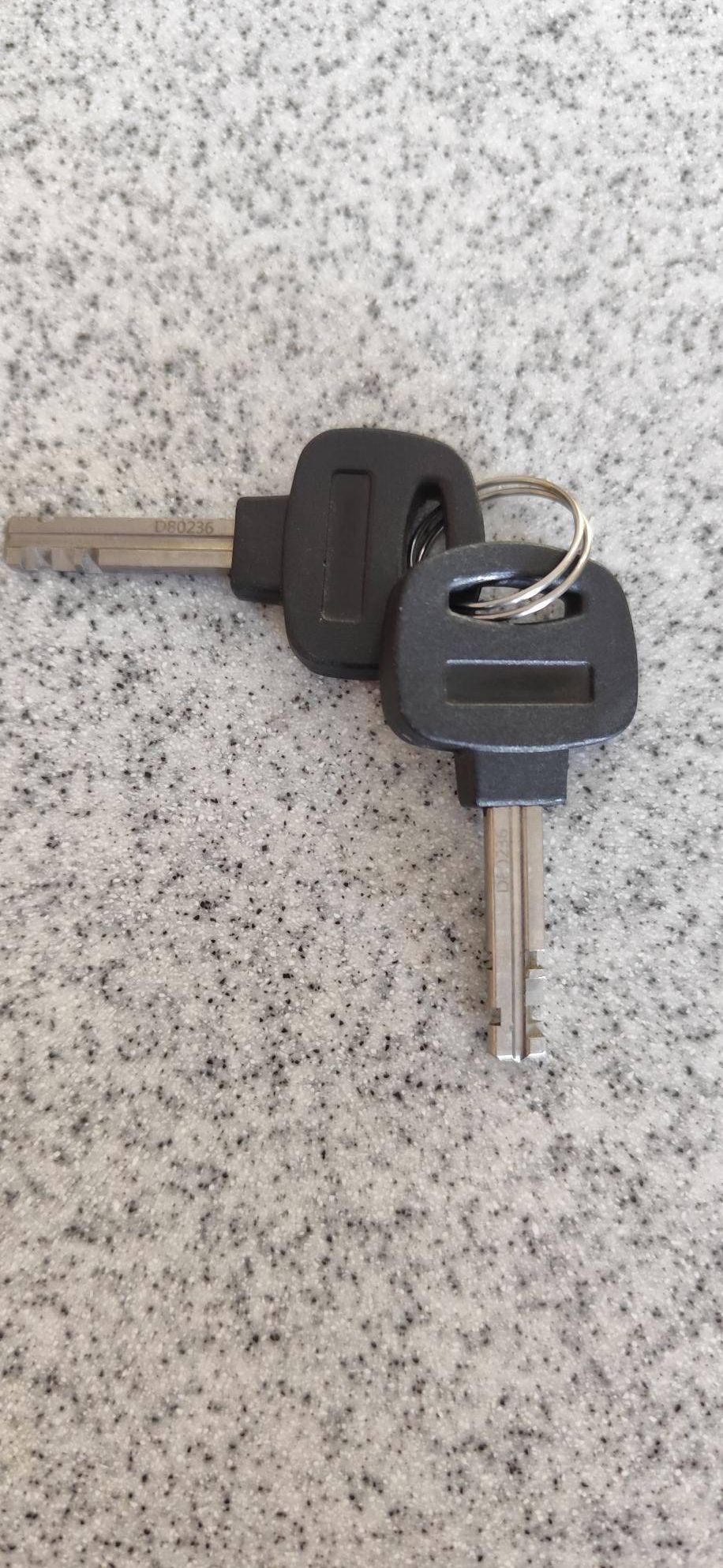 Two car keys with black plastic key fobs and silver blades, one labeled D80236 and the other D80238, placed on a marble surface.
