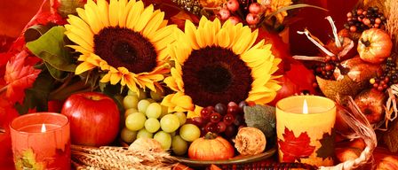 Ein Tisch mit Herbstfrüchten, Sonnenblumen und zwei brennenden Kerzen mit Herbstblättern.