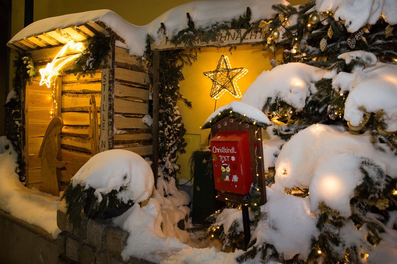 Eine weihnachtliche Ausstellung mit einer Holzhütte, schneebedeckten Bäumen und einem beleuchteten Stern. Ein roter Postkasten mit der Aufschrift Christkindl Post ist mit Weihnachtsdekorationen geschmückt.
