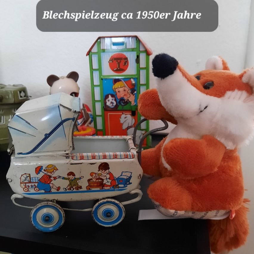 Eine alte Blechspielzeug-Babywagen mit einem Fuchs-Plüschtier in der Nähe, umgeben von anderen Spielzeugen vor weißem Hintergrund.