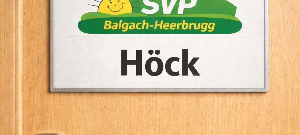 Eine Tür mit einer Namenstafel, die SVP Balgach-Heerbrugg Hock zeigt, mit einem grünen Hut, einer Sonne und einer Schweizer Flagge.