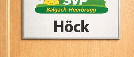 Eine Holztür mit einem silbernen Griff zeigt ein Schild darüber. Das Schild trägt den Text SVP Balgach-Heerbrugg Höck. Auf dem Schild sind eine Sonne und eine Schweizer Flagge abgebildet.