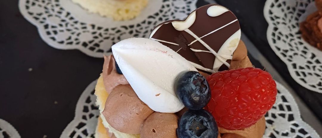 Mehrere mit Schokolade überzogene Desserts, gekrönt mit Sahne, Beeren und einem herzförmigen Schokoladendeckel, sind auf einem Tisch mit Spitzenservietten angeordnet.