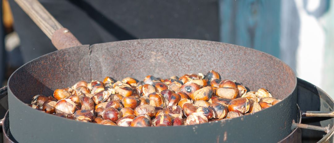Eine Pfanne voller gerösteter Kastanien auf einem Grill, einige noch mit Schale.