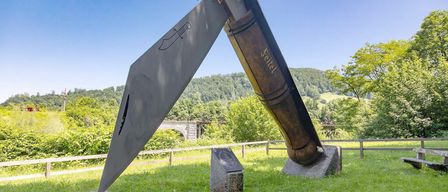 Eine große Outdoor-Skulptur eines Messers steht in einem Grasfeld. Die Klinge ist silber und der Griff braun.