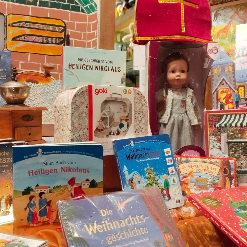 Eine Auswahl an weihnachtlich dekorierten Artikeln, darunter Bücher, eine Puppe und eine Kaffeemühle, sind ordentlich auf einem Tisch angeordnet.