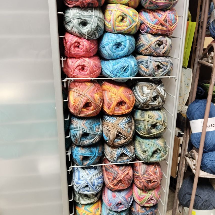 Ein Schrank voller bunter Wollknäuel, jedes Knäuel ordentlich gewickelt. Der Schrank hat mehrere Regale und die Wollknäuel sind in Reihen angeordnet.