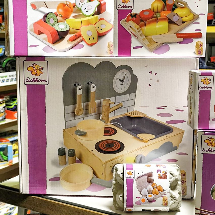 Zwei Spielzeugboxen für eine Kinderküche, eine mit einem Schneidebrett und Früchten, die andere mit Herd und Spüle.