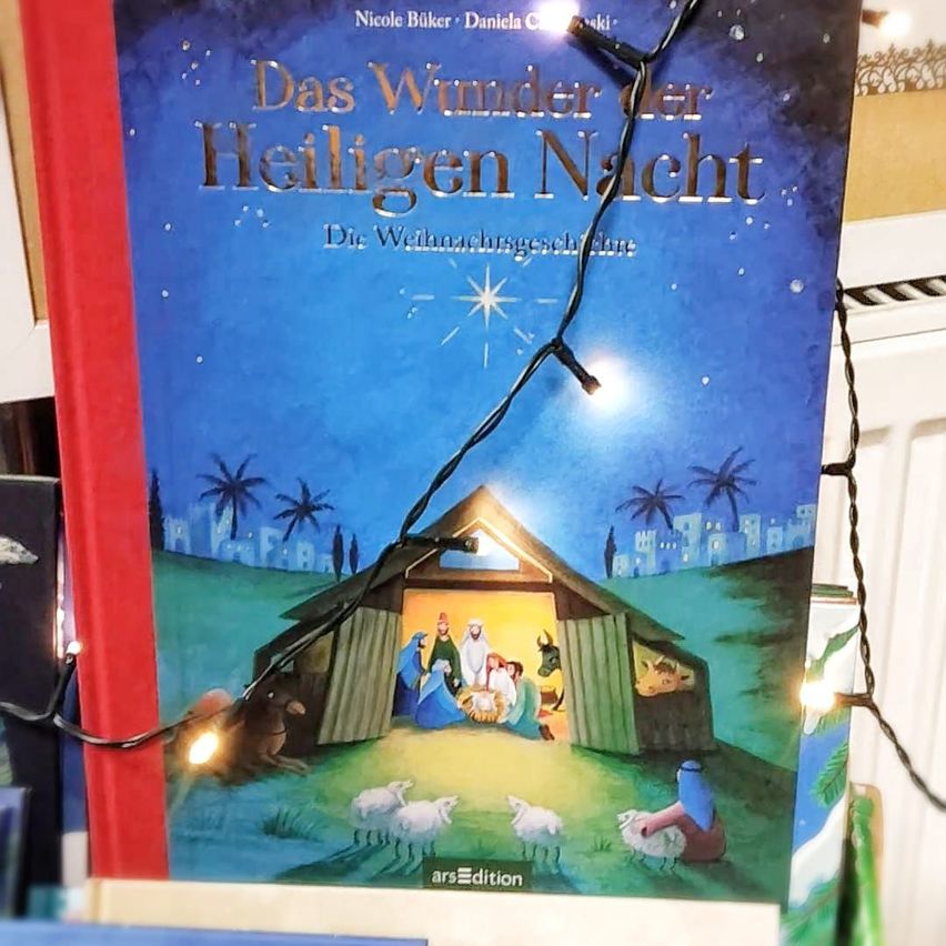 Das Buchcover 'Das Wunder der Heiligen Nacht' zeigt eine Krippenszene mit Maria, Josef und dem Jesuskind in einer Scheune, umgeben von Tieren und Palmen, mit Lichterketten, die die Szene erhellen.