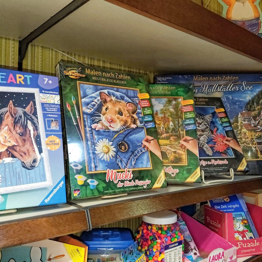 Ein Holzregal zeigt eine Vielzahl von Puzzles, darunter ein Pferd, eine Katze und ein Hamster, alle mit farbenfrohen und detaillierten Illustrationen. Die Puzzles stammen aus verschiedenen Serien und haben eine unterschiedliche Anzahl von Teilen.