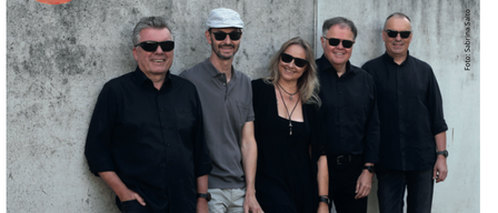 Ein Werbebild für eine Veranstaltung mit einer Gruppe von fünf Personen in schwarzer Kleidung. Das Datum und die Uhrzeit der Veranstaltung sind prominent angezeigt.