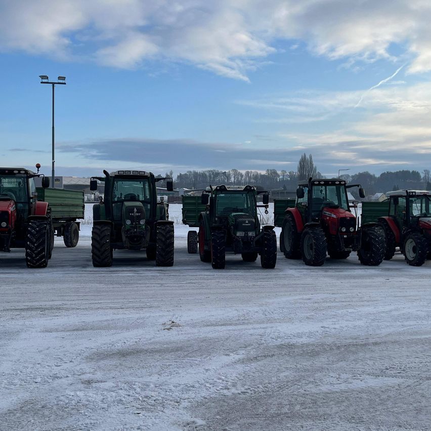 Fünf Traktoren sind auf einem verschneiten Feld geparkt, zwei sind rot und drei grün. Der Himmel ist blau mit einigen Wolken.